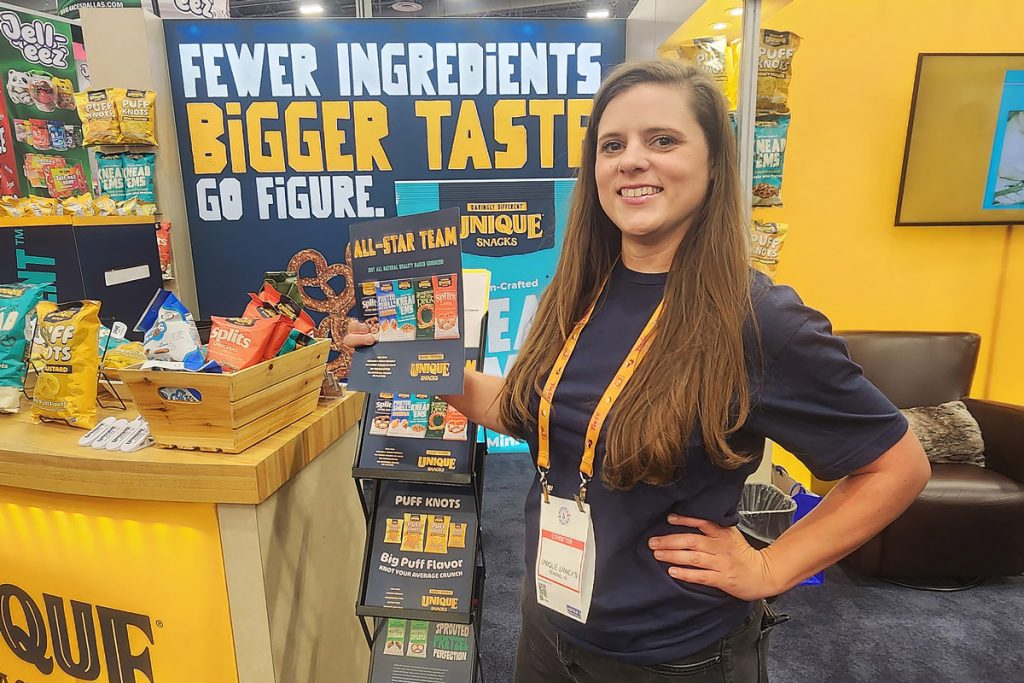 Promotional staff member showcasing snacks at a trade show booth for Unique Snacks.