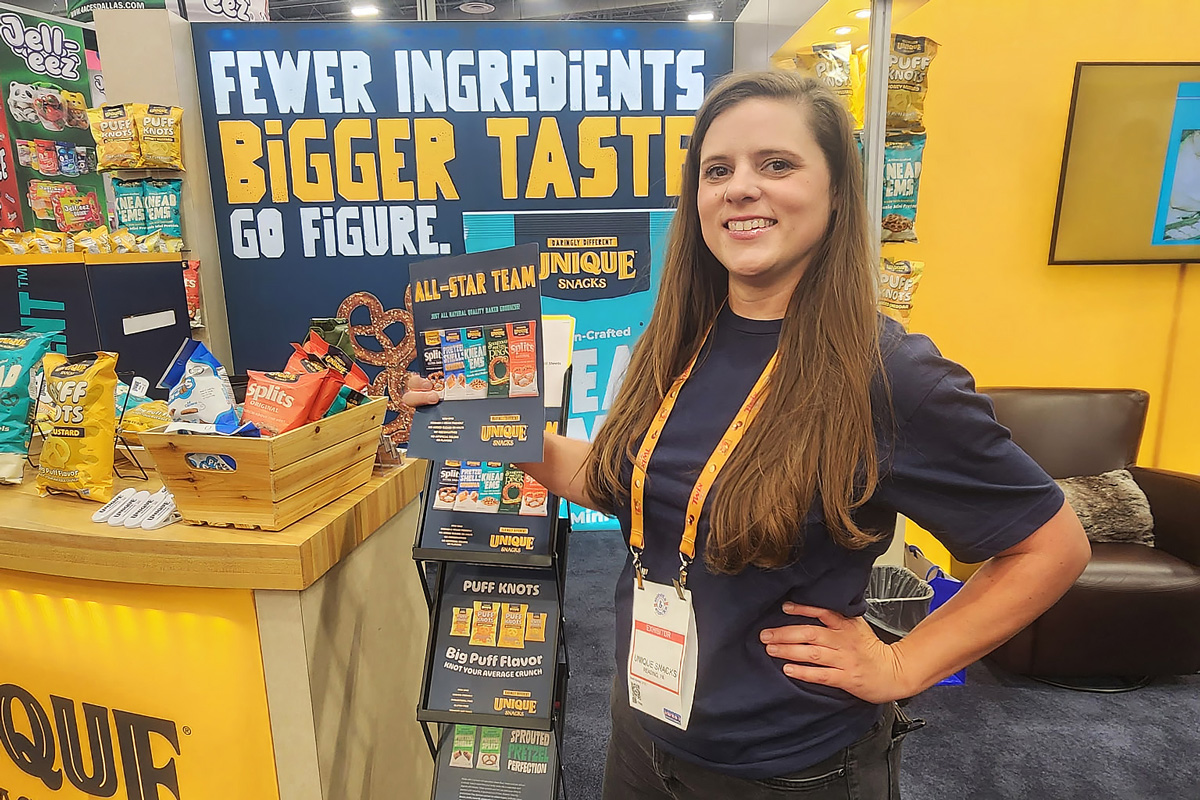 Promotional staff member showcasing snacks at a trade show booth for Unique Snacks.